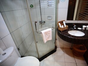 A bathroom with a glass shower enclosure, a white toilet, a sink with toiletries, and a mirror.