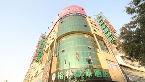 A hotel with a curved facade, multiple floors, and a prominent green sign indicating it is a hotel. - GreenTree Inn Huaian Chuzhou Avenue Zhou Enlai Memorial Hall Hotel (Huai'an)