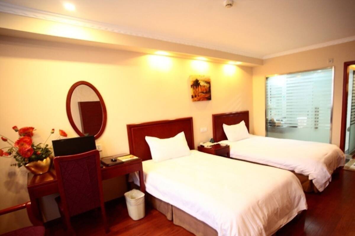 A hotel room with two beds, a desk with a chair, a mirror, and a window with blinds.