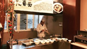 A chef preparing food in a kitchen with a large menu board above the counter. - GreenTree Inn Huaian Chuzhou Avenue Zhou Enlai Memorial Hall Hotel (Huai'an)