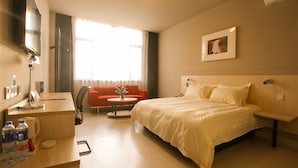 Ein Hotelzimmer mit Bett, Schreibtisch, Stuhl, Fernseher und einem Fenster mit Vorhängen.