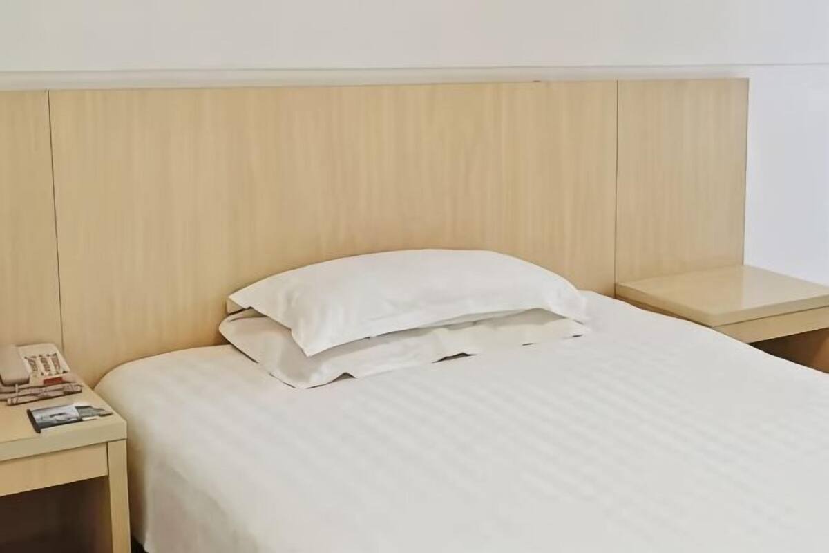 A neatly made bed with a white pillow and a wooden headboard.