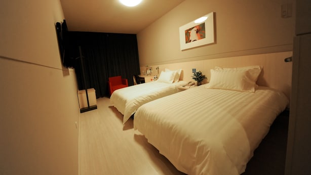 Ein Hotelzimmer mit zwei Betten, einem Schreibtisch, einem Stuhl, einem Nachttisch und einer Deckenleuchte.
