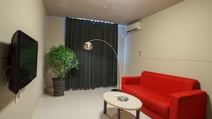 Ein kleiner, moderner Wohnraum mit einem roten Sofa, einem runden Tisch, einem Blumentopf, einem Fernseher und einer Deckenleuchte.