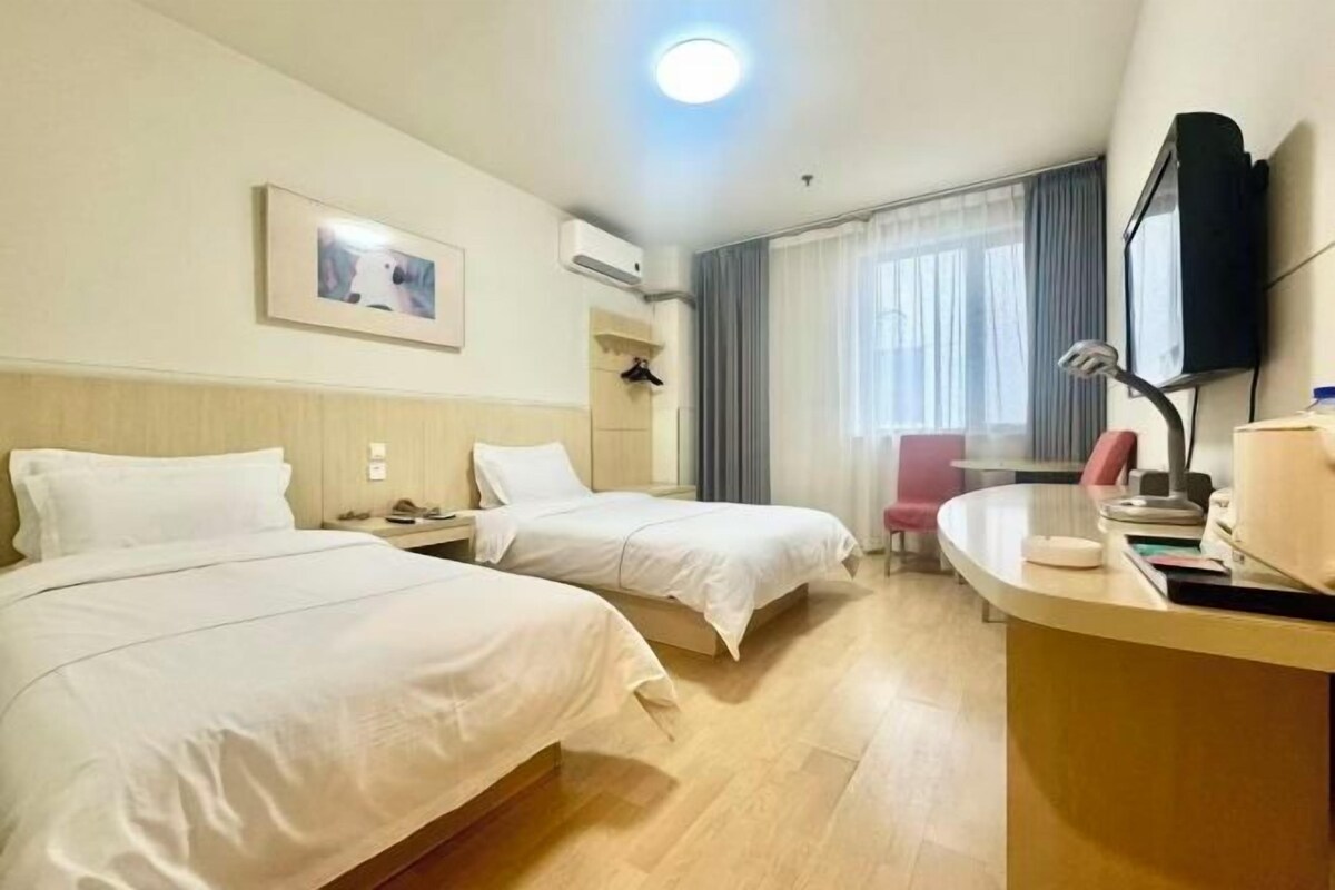A hotel room with two beds, a desk, a chair, a TV, and a window with curtains.
