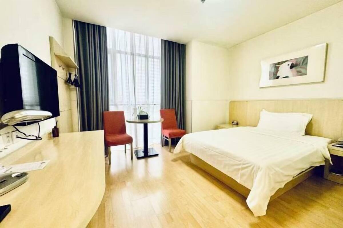 A hotel room with a bed, a desk with a chair, a TV, and a window with curtains.