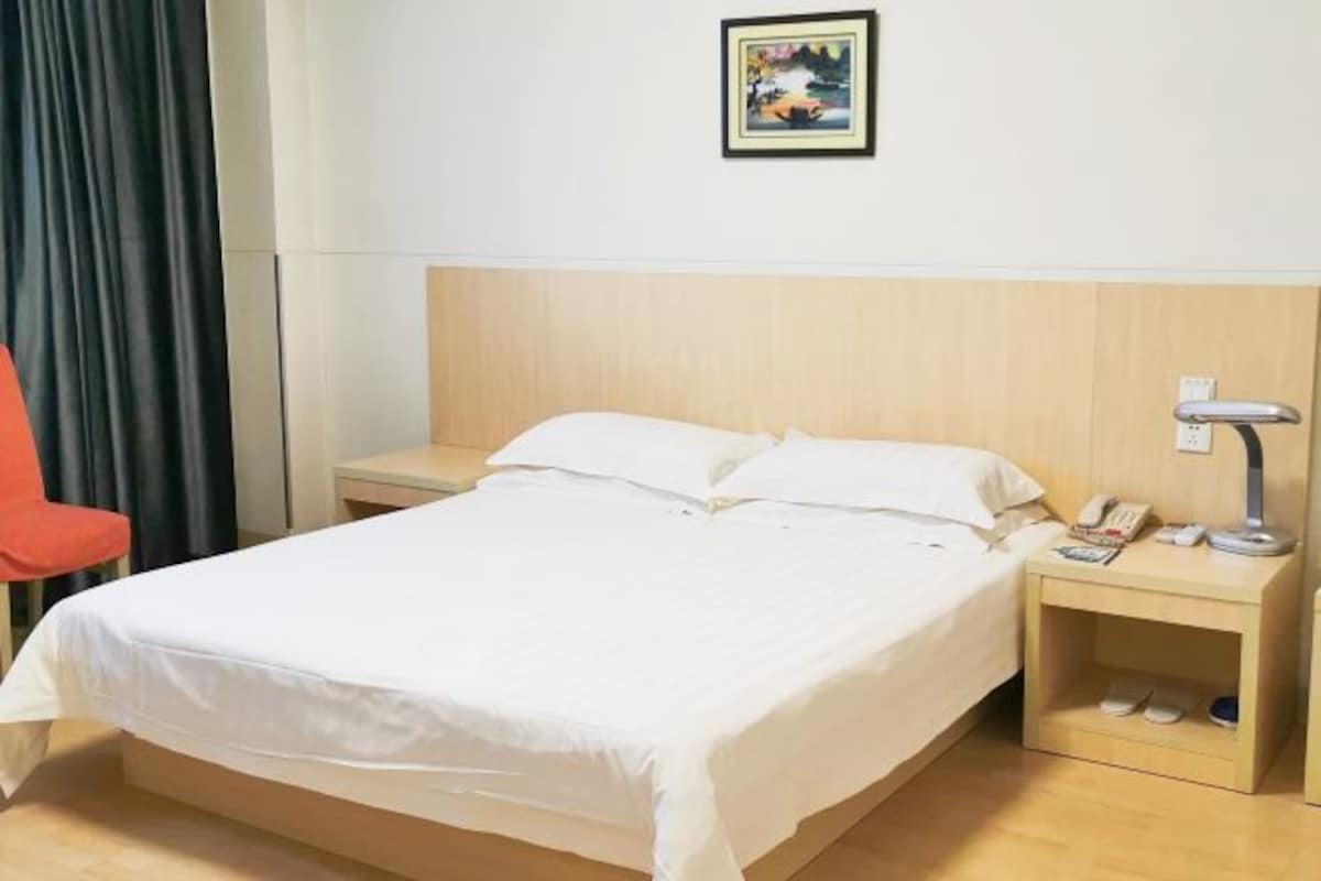 A hotel room with a bed, a nightstand, a lamp, a phone, and a pair of slippers.