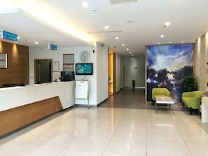A hotel reception area with a reception desk, a clock, a digital screen, and a mural on the wall. - Jinjiang Inn Taicang Shanghai Lu (Suzhou)