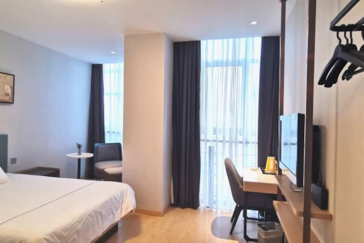 A hotel room with a bed, a desk, a chair, a TV, and a window with curtains.
