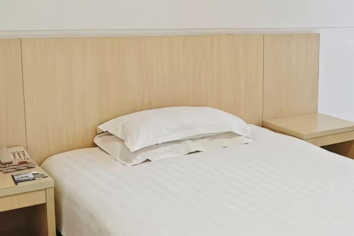 A neatly made bed with a white pillow and a wooden headboard.