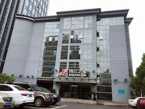 A modern building with a large glass facade, a prominent signage for 'Jinjiang Inn,' and a parking lot with several cars. - Jinjiang Inn Taicang Shanghai Lu (Suzhou)