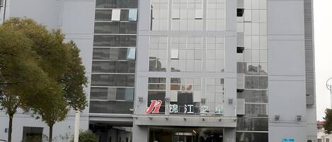 Um edifício moderno com fachada de vidro, um letreiro com caracteres chineses e uma área de estacionamento com carros.