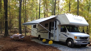A white RV with a large awning parked in a forested area. - Lake Wanoka Resort (Honesdale)