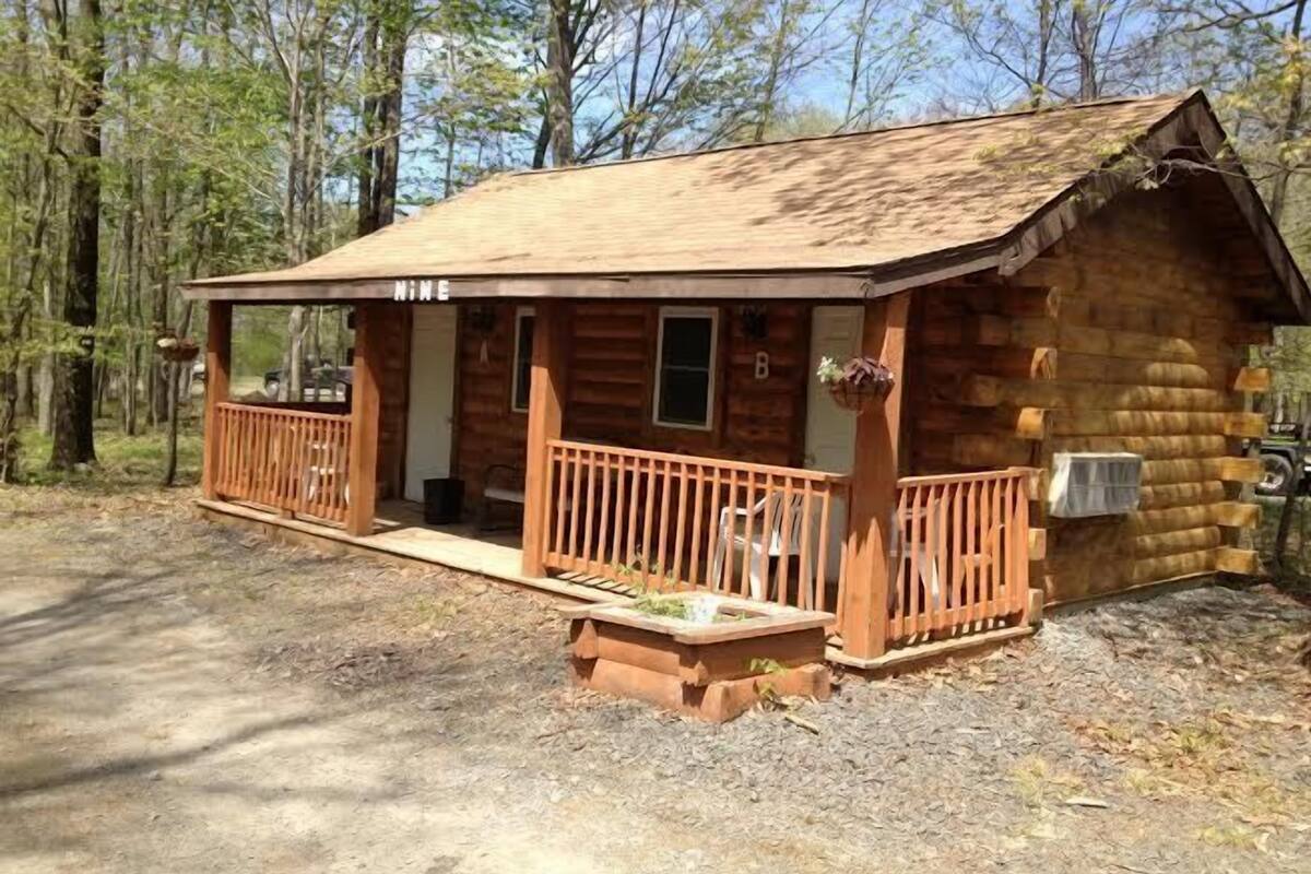 A log cabin with a porch and a small deck, surrounded by trees.