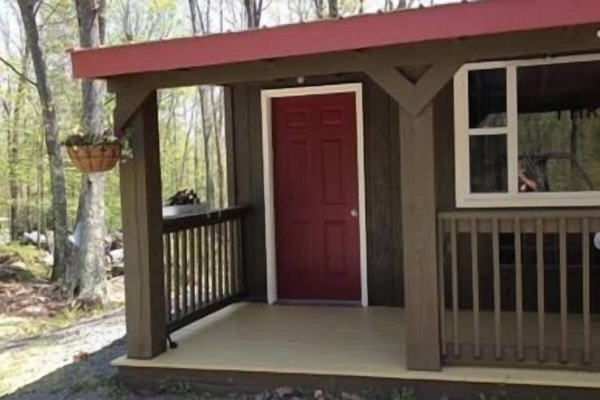 A cabin with a red door, a wooden porch, and a hanging basket.