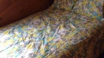 A bed with a floral-patterned bedspread and matching pillows in a room with wooden walls.