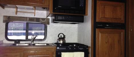 A compact kitchen with wooden cabinets, a microwave, a stove, and a window.