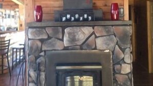 A stone fireplace with a metal insert, two red vases on top, and a wooden ceiling with exposed beams. - Lake Wanoka Resort (Honesdale)