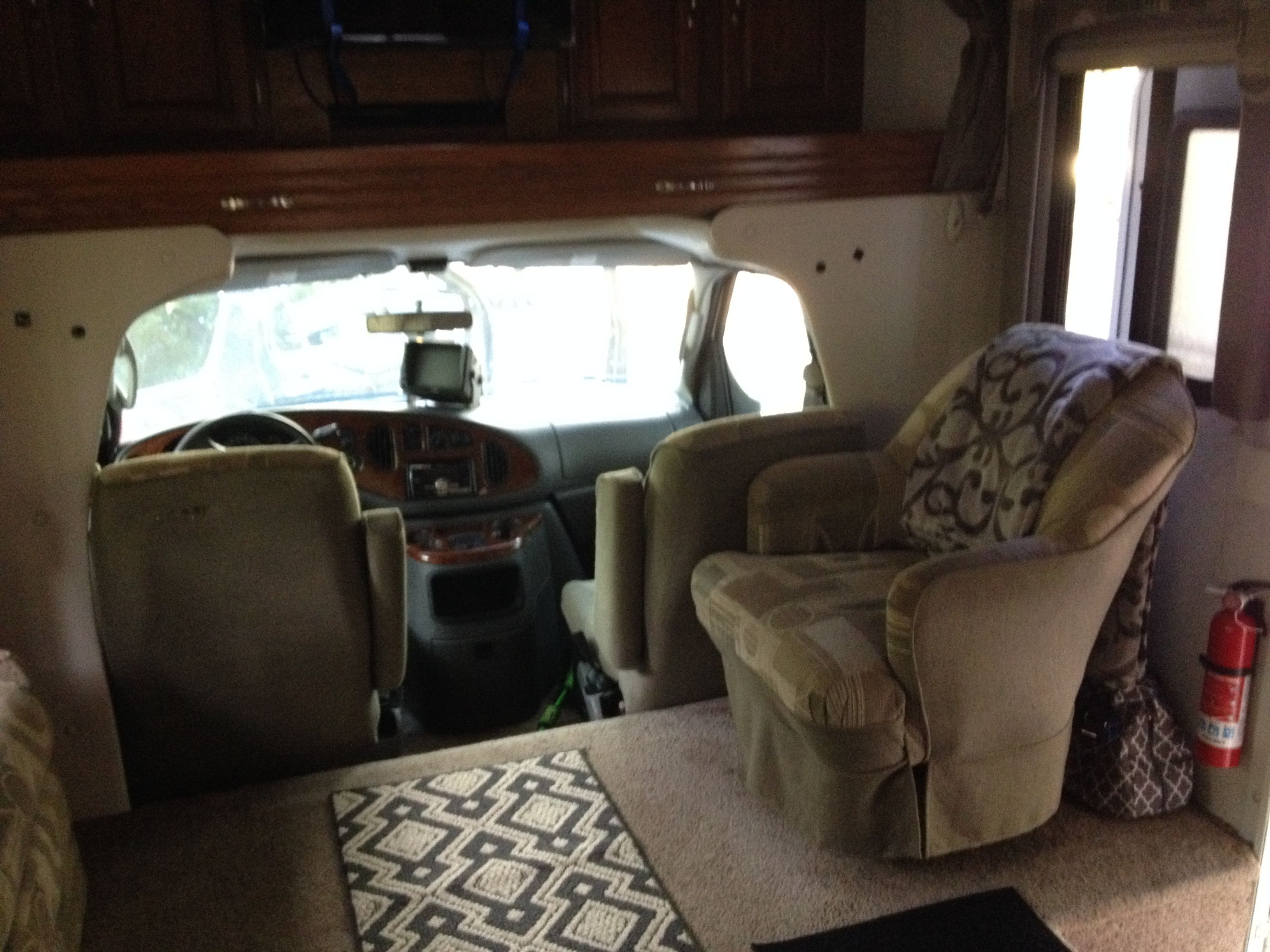 A compact RV interior with a kitchenette, a patterned rug, and a cushioned seating area.