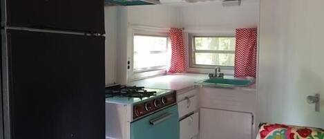 A compact kitchen with a black refrigerator, teal stove, and white cabinets.