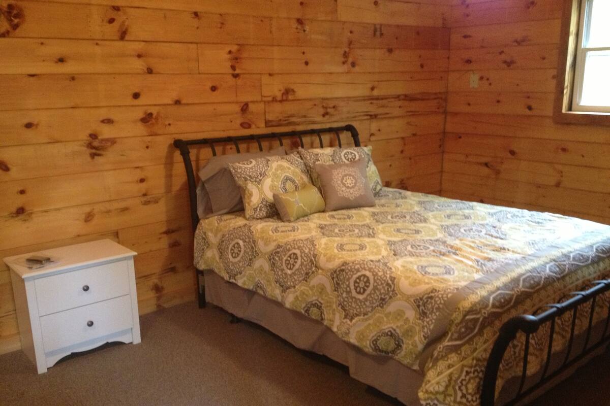 A wooden-paneled room with a bed, a nightstand, and a window.