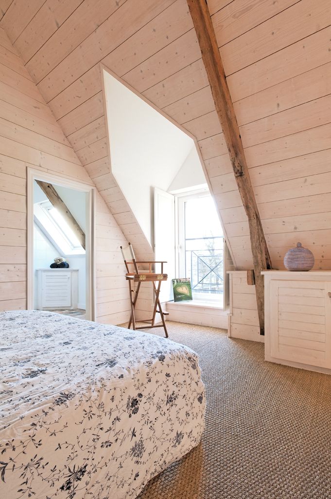 A bedroom with a sloped ceiling, a bed with a floral bedspread, a chair, and a window with a view.