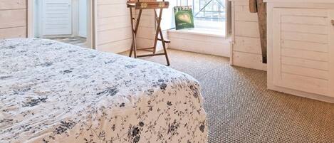 A bedroom with a sloped ceiling, a bed with a floral bedspread, a chair, and a window with a view.