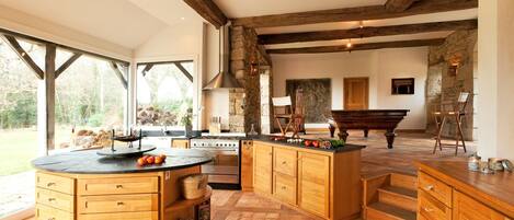 A spacious kitchen with wooden cabinetry, a central island, and a piano in the background.