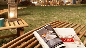 Um edifício de pedra com um alpendre coberto, um banco de madeira, uma mesa com um candeeiro e uma revista.
