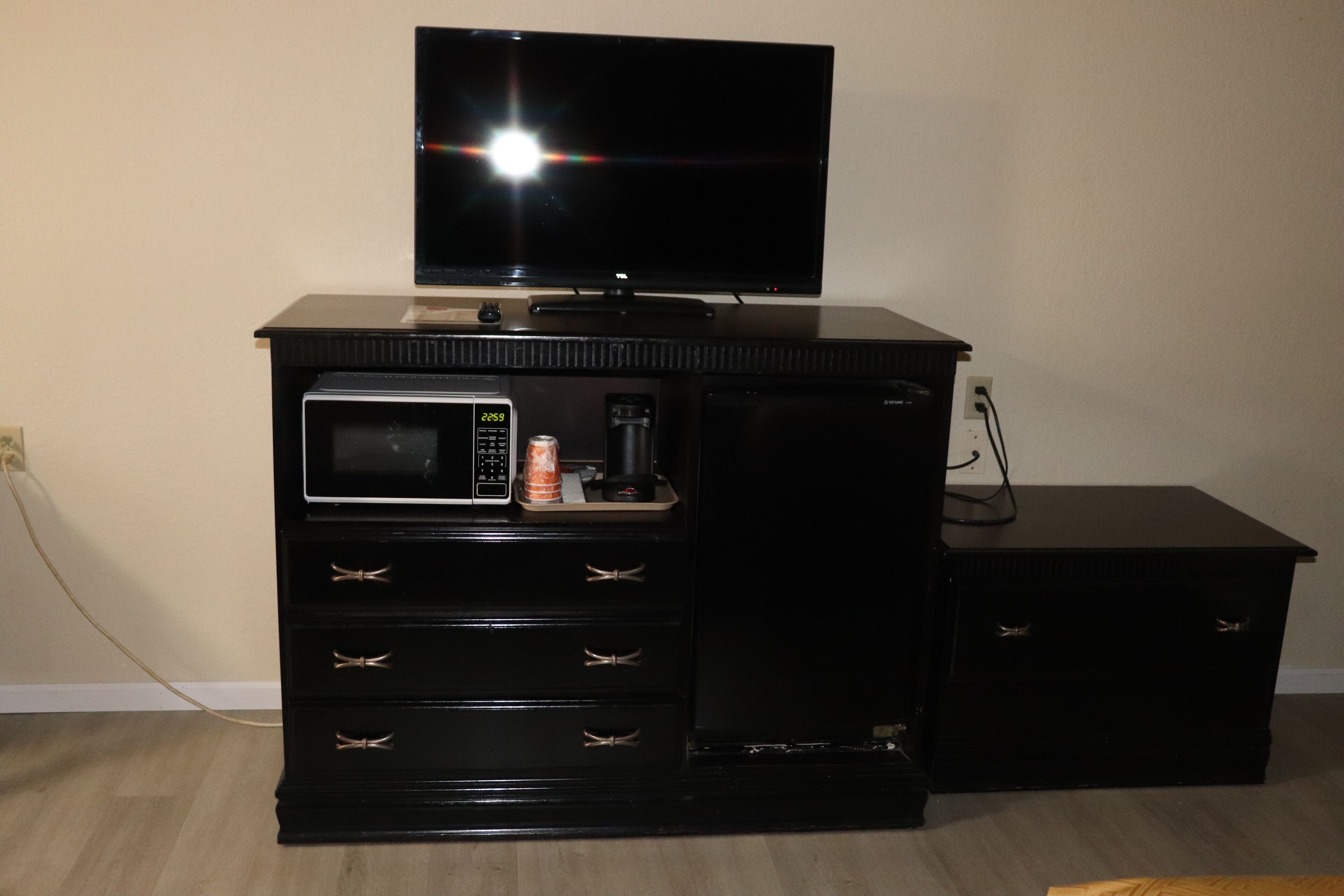 A black entertainment center with a TV, microwave, and a small refrigerator.