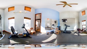 Vista panorámica de un gimnasio en casa con equipo de ejercicio, una caminadora y una silla.