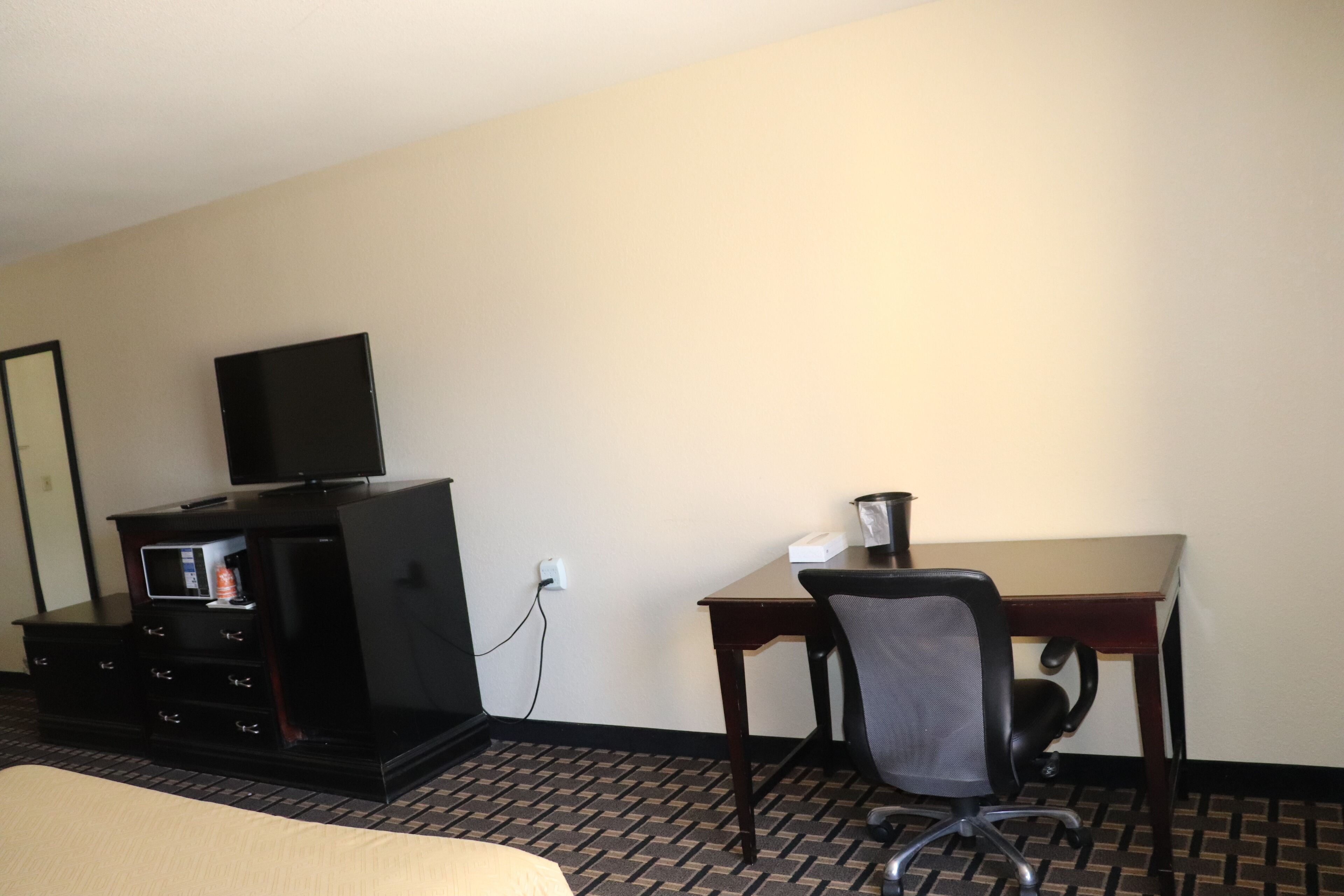 A hotel room with a bed, a desk, a chair, a television, and a minibar.