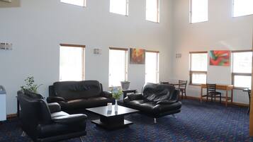 A spacious living area with a blue patterned carpet, black leather sofas, a coffee table, and a dining table with chairs.