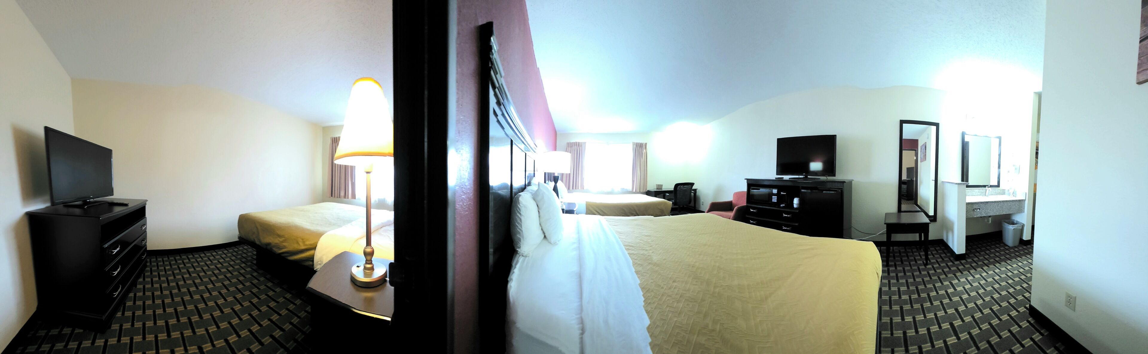 A hotel room with two beds, a desk, a TV, a lamp, and a dresser.