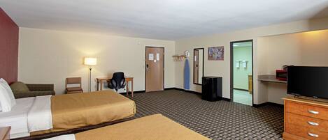 Habitación de hotel con dos camas, un escritorio, una silla, un televisor y un baño visible a través de una puerta abierta.