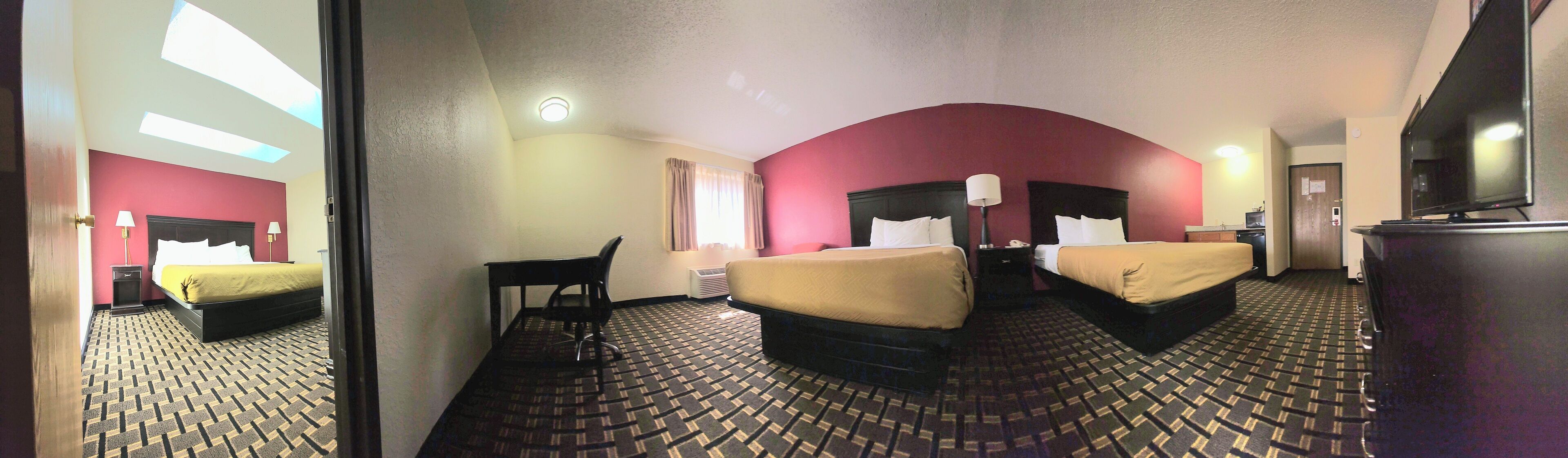 A hotel room with two beds, a desk, a chair, a television, and a patterned carpet.