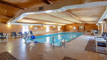 An indoor swimming pool with a tiled floor, surrounded by lounge chairs and a wooden ceiling.
