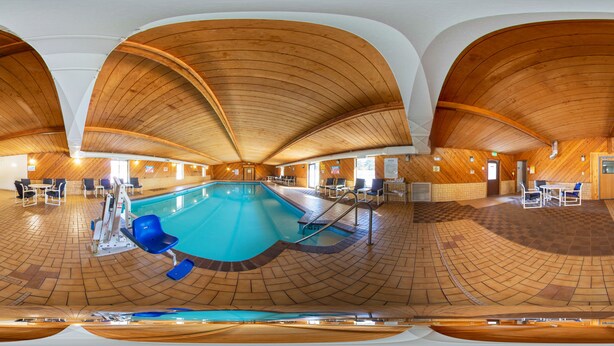 Vista panorámica de un área de piscina con techo de madera, asientos junto a la piscina y un piso con estampado de cuadros.