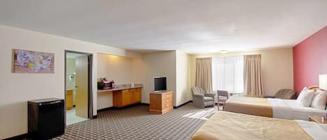 A hotel room with a bed, a desk with a television, a chair, and a small kitchenette.