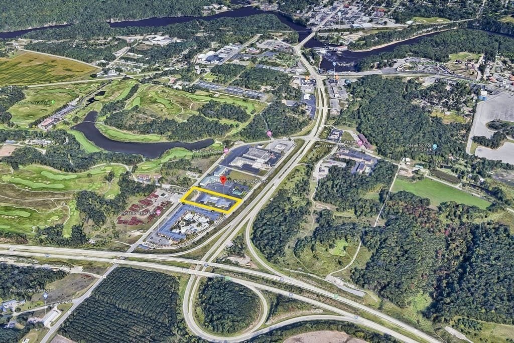 An aerial view of a golf course with multiple greens, a large parking area, and surrounding wooded areas.