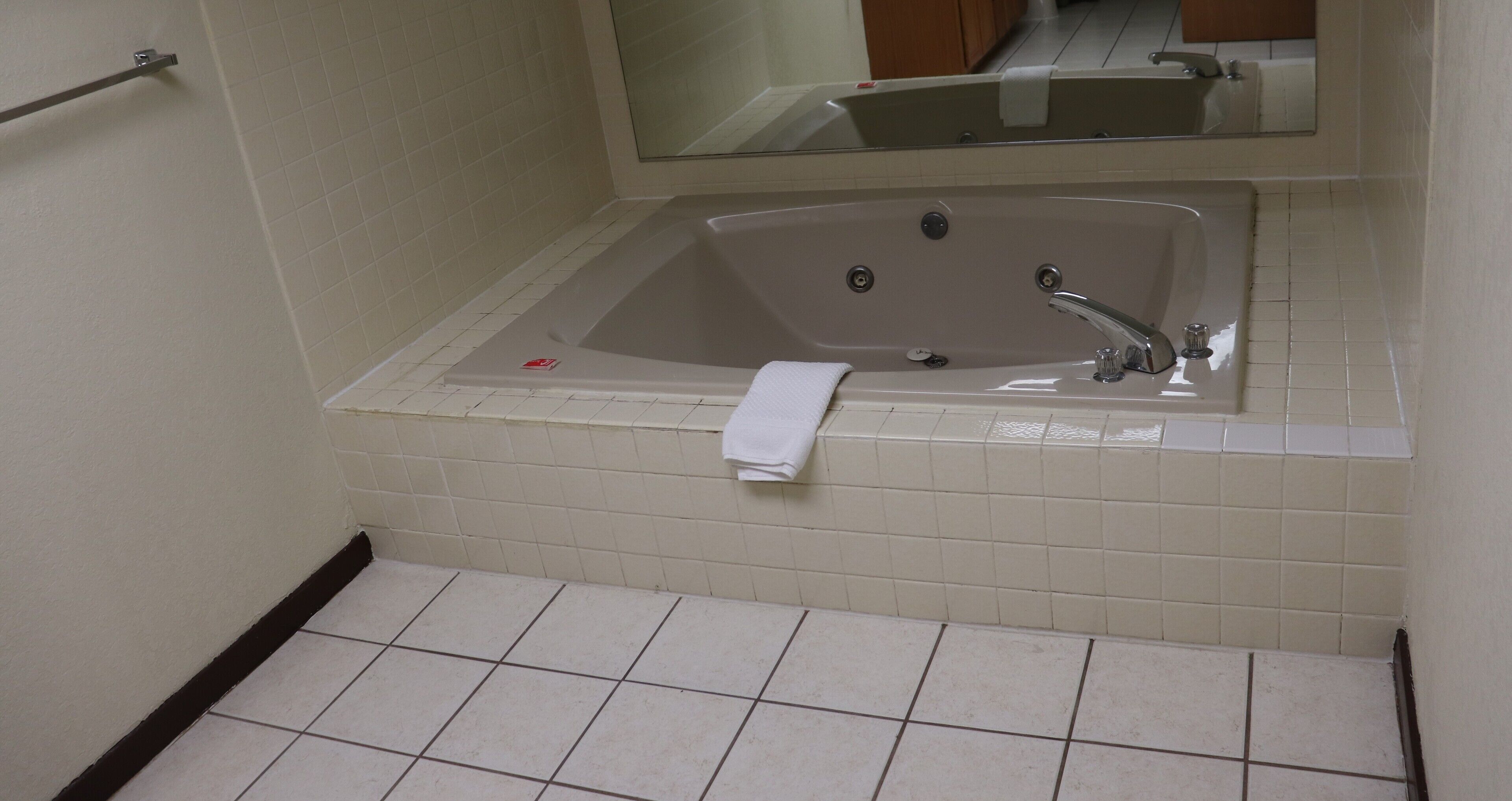 A bathroom with a large bathtub, a towel hanging on the wall, and a mirror above the tub.