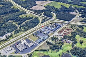 An aerial view of a commercial area with a large parking lot, a building with a flat roof, and a golf course.