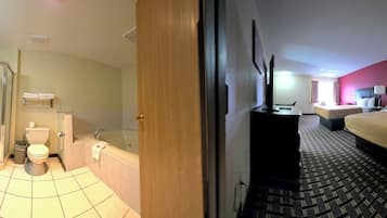 Een hotelbadkamer met douche, toilet en wastafel. De kamer heeft een bed en een bureau met stoel.