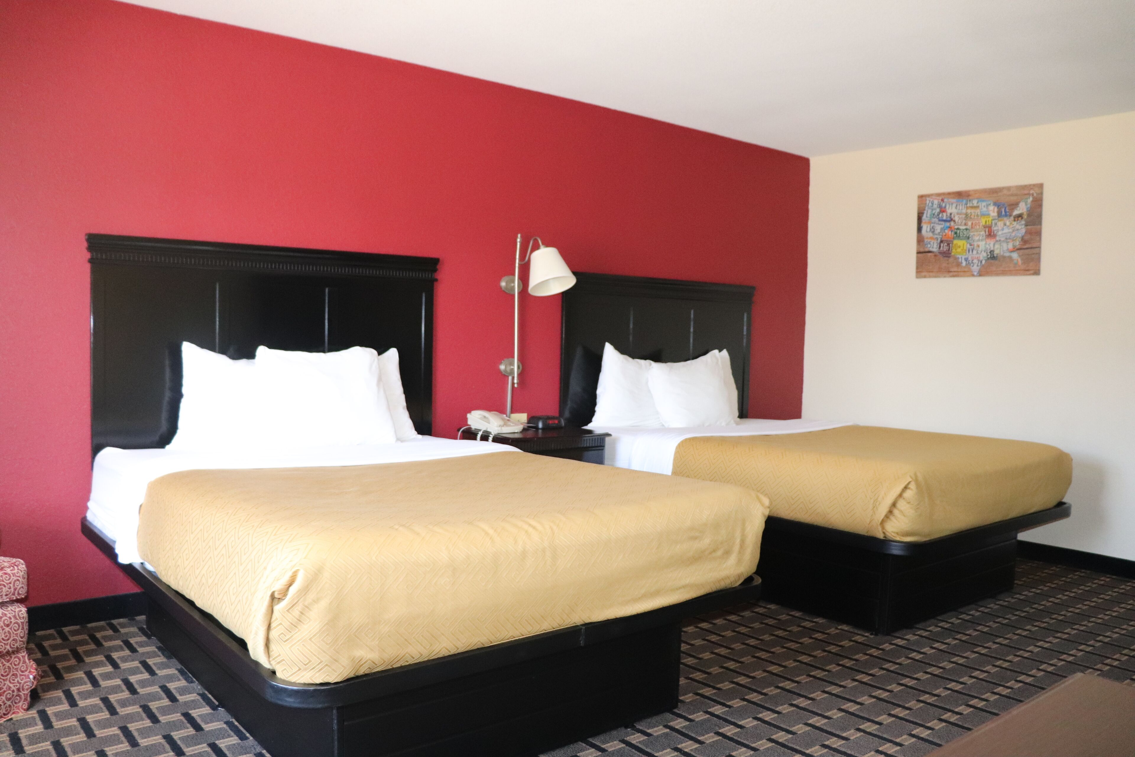 A hotel room with two beds, a red wall, a map on the wall, and a patterned floor.
