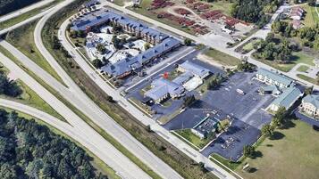 An aerial view of a commercial area with a large building, parking lots, and surrounding greenery.