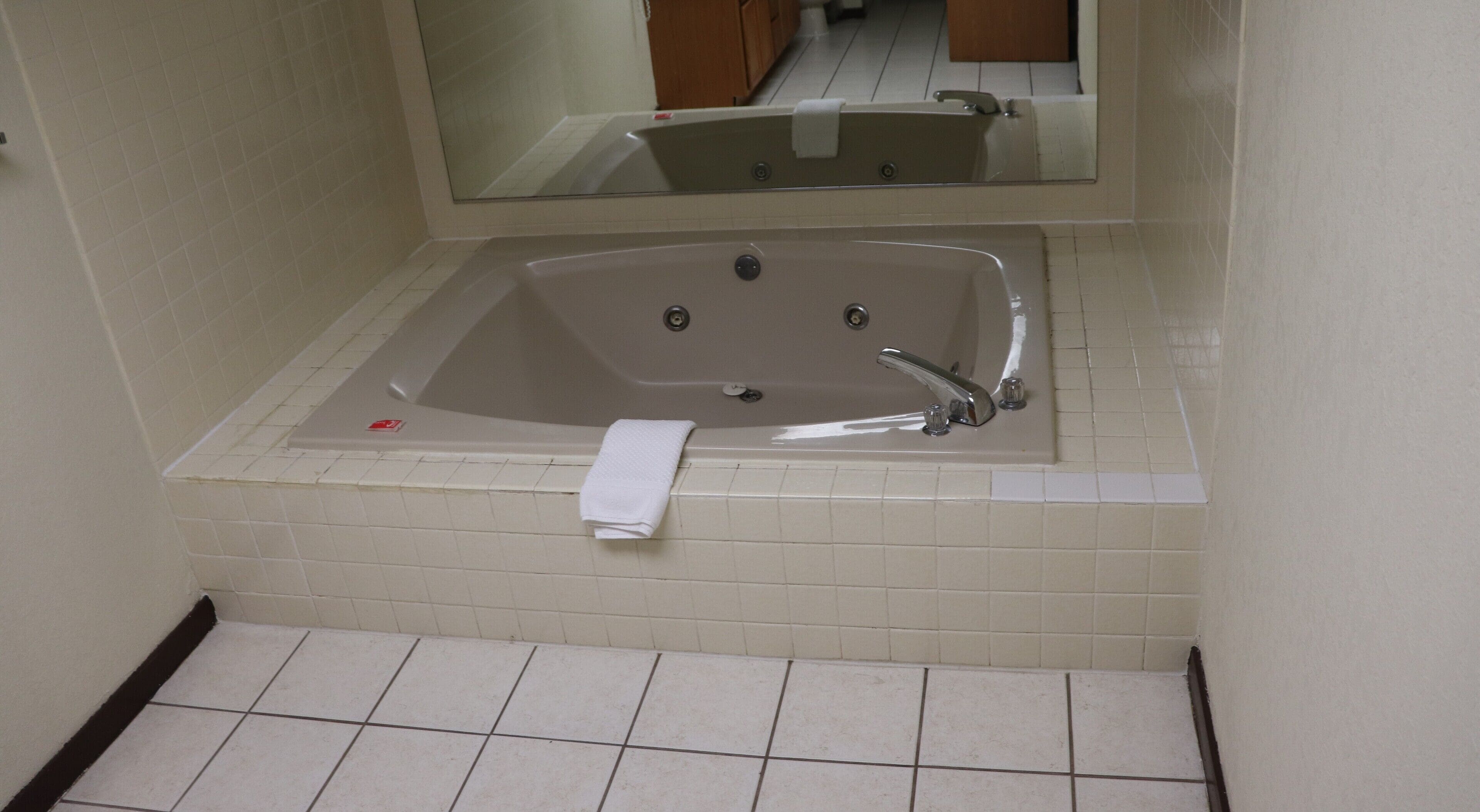 A bathroom with a large bathtub, a mirror above it, and a tiled floor.
