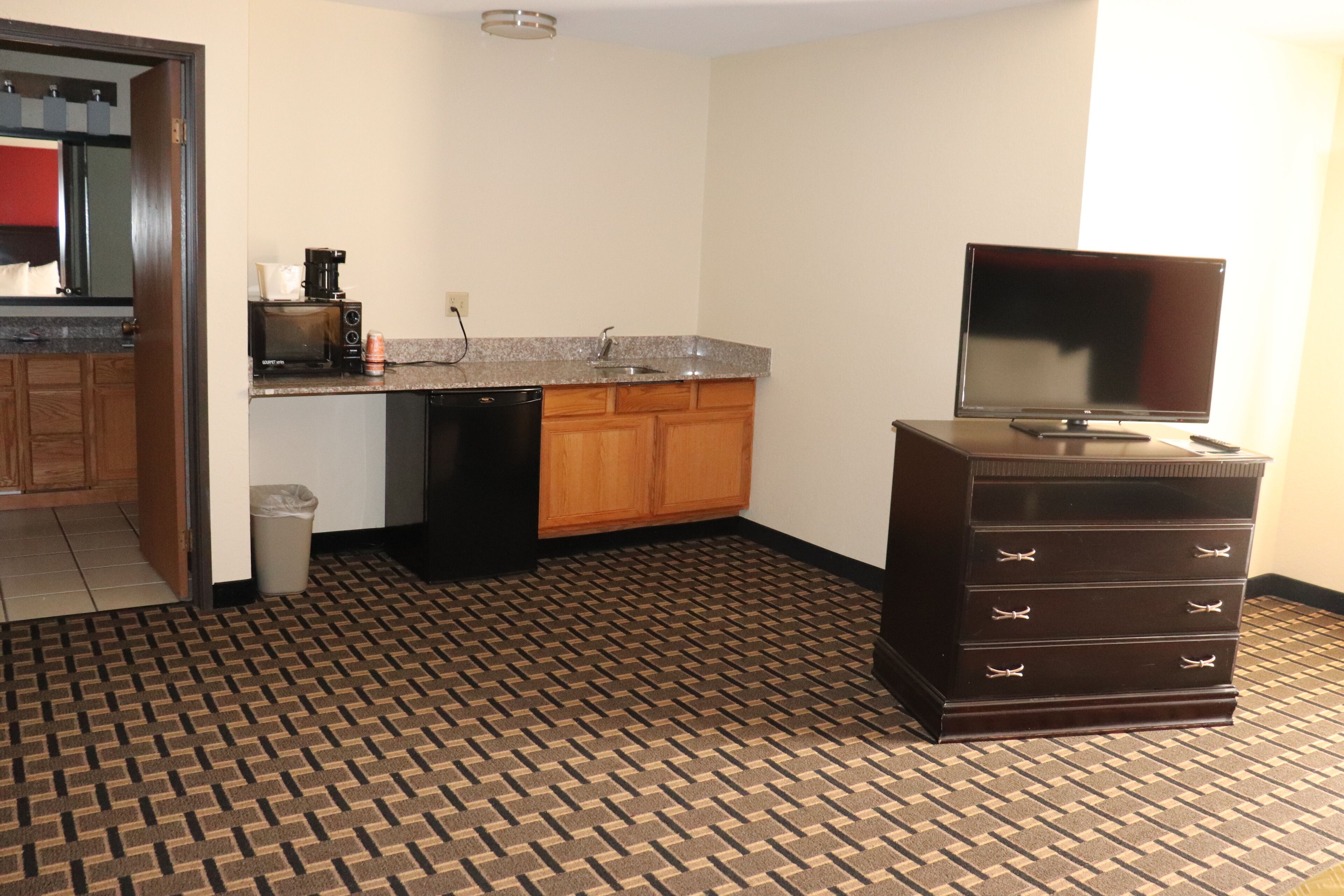 A compact kitchen with a microwave, coffee maker, and a TV on a dresser.