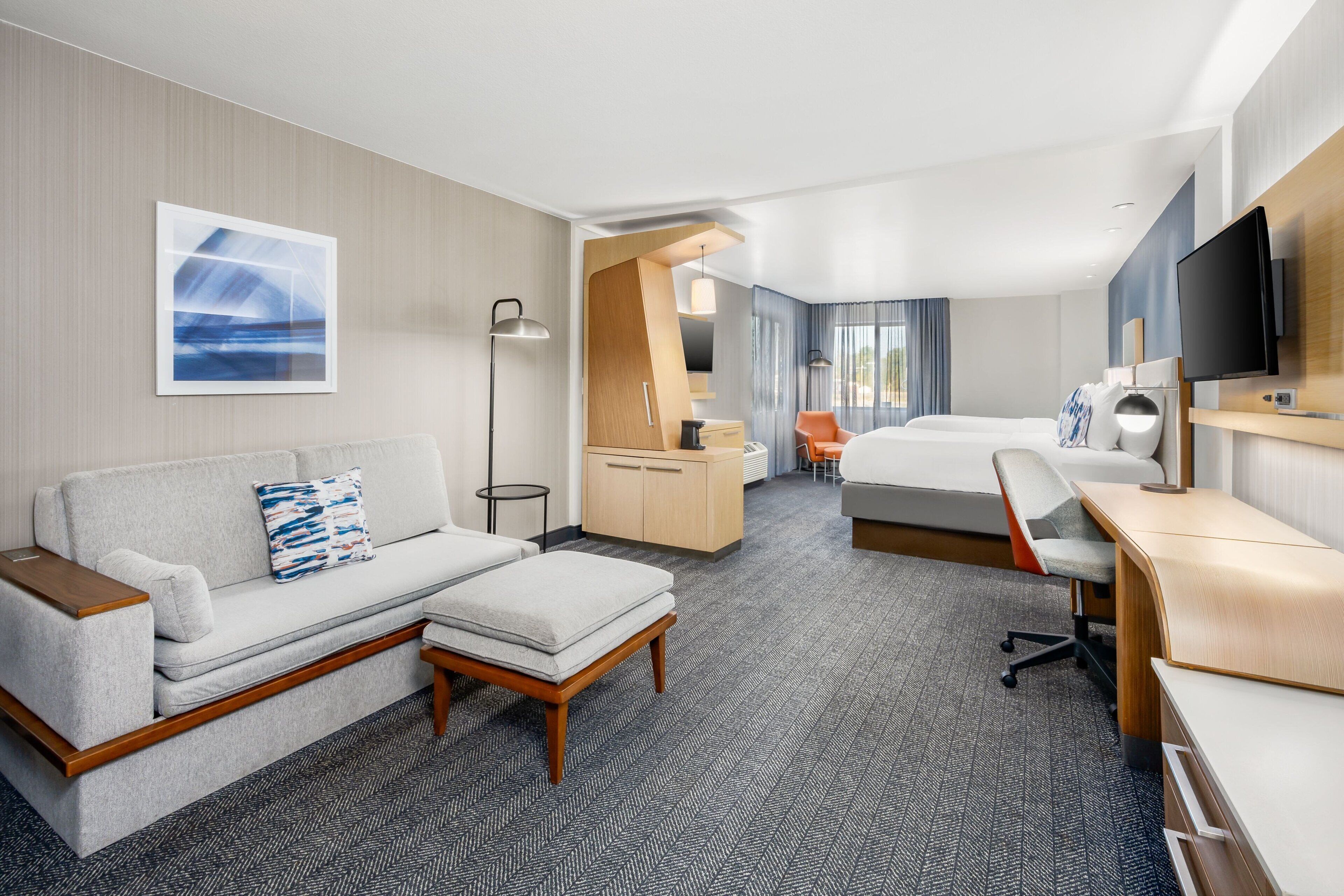 A modern hotel room with a sofa, a desk, a bed, and a television.