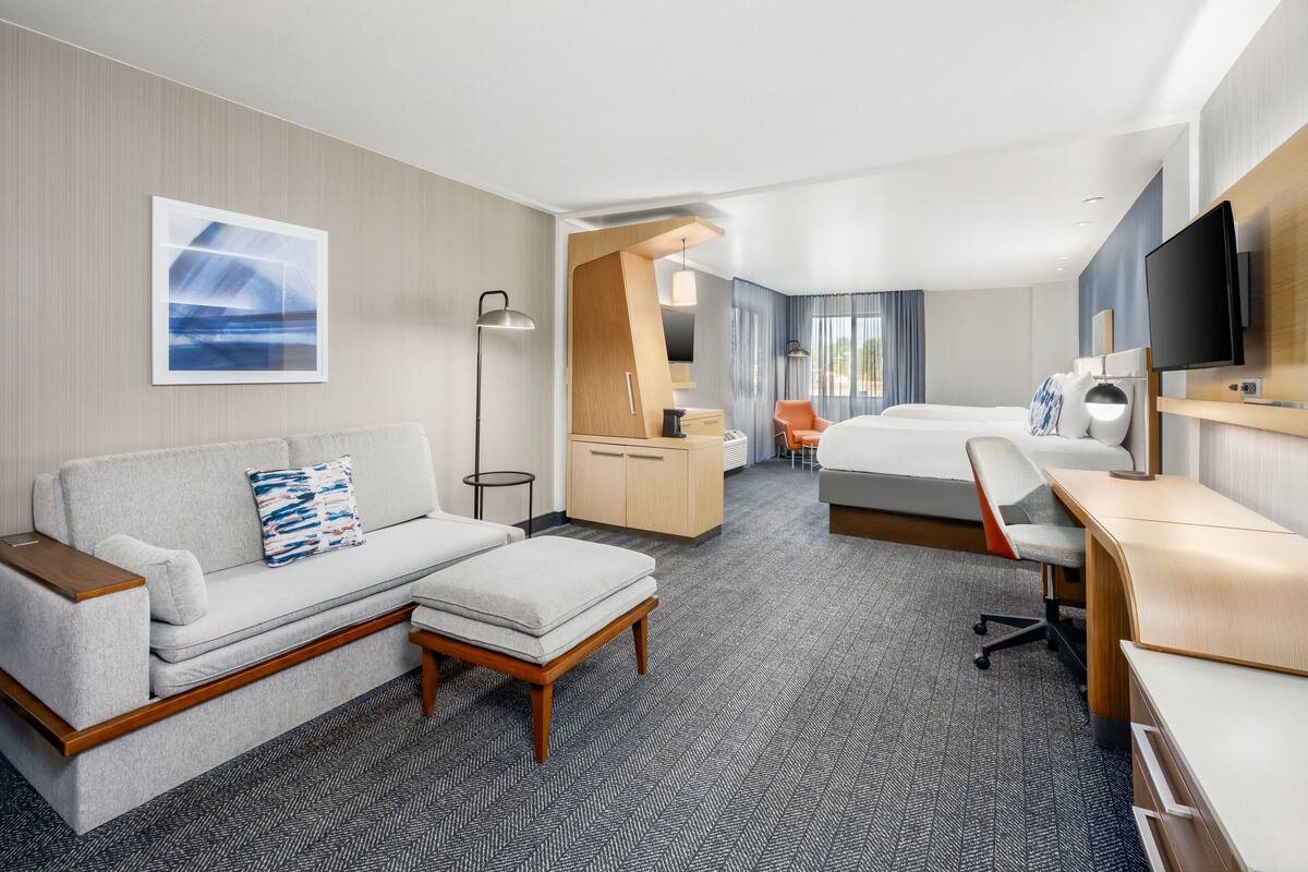 A modern hotel room with a sofa, a desk, a bed, and a television.