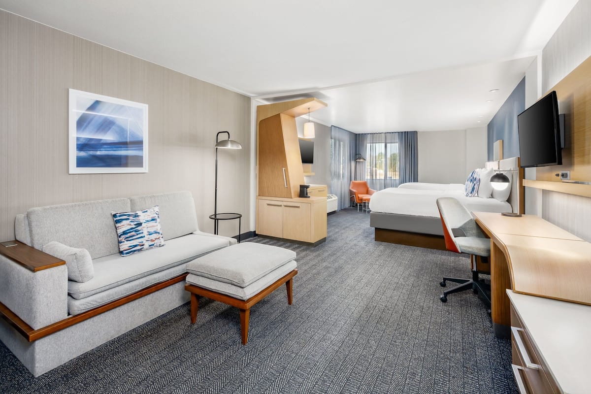 A modern hotel room with a sofa, a desk, a bed, and a television.